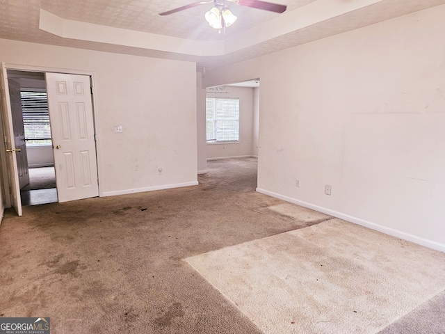 unfurnished room with a tray ceiling, ceiling fan, carpet floors, and a healthy amount of sunlight