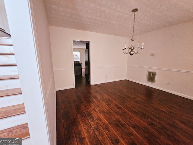 unfurnished dining area featuring a textured ceiling, an inviting chandelier, and dark wood-type flooring