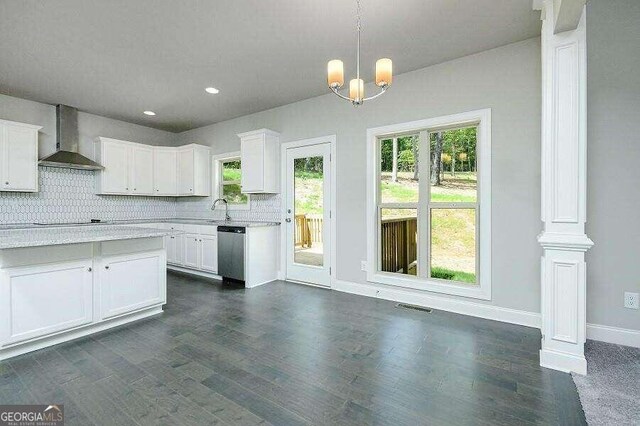 kitchen with wall chimney range hood, dishwasher, hanging light fixtures, and white cabinets