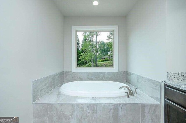 bathroom with vanity and tiled bath