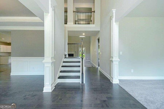 stairs with ornate columns, ornamental molding, hardwood / wood-style flooring, and a high ceiling