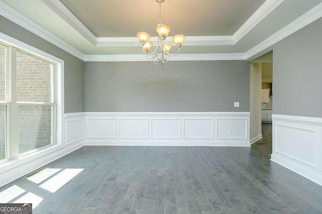 empty room with wood finished floors, ornamental molding, a wainscoted wall, a notable chandelier, and a tray ceiling