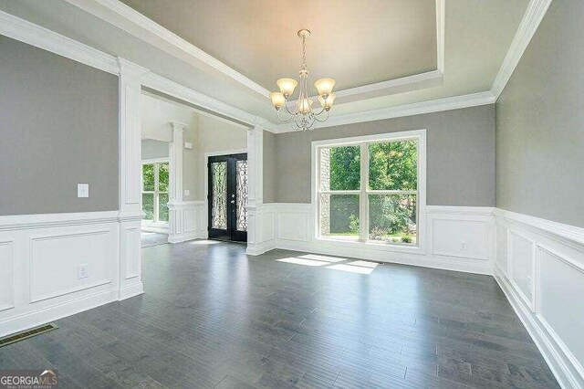 empty room with decorative columns, dark hardwood / wood-style flooring, a chandelier, a tray ceiling, and french doors