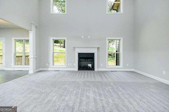 unfurnished living room featuring a towering ceiling, plenty of natural light, and carpet floors