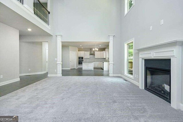 unfurnished living room featuring dark carpet and decorative columns