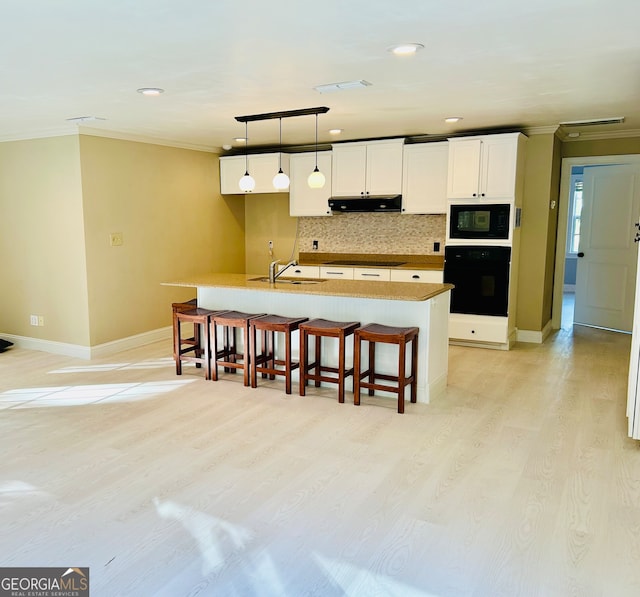 kitchen featuring white cabinetry, light hardwood / wood-style flooring, backsplash, a kitchen island with sink, and black appliances