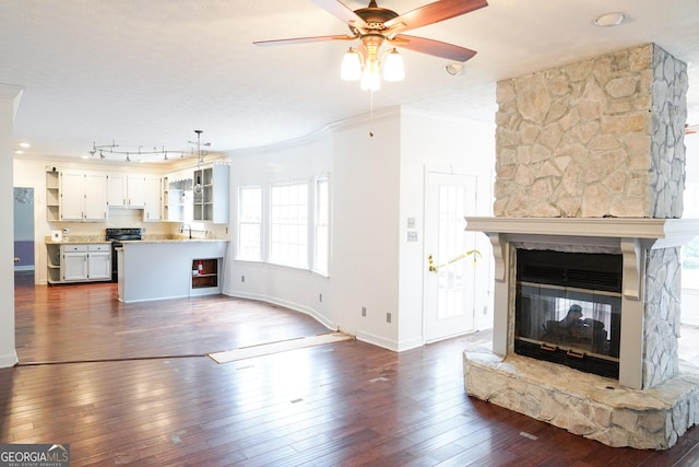 unfurnished living room with ceiling fan, sink, a stone fireplace, dark hardwood / wood-style flooring, and ornamental molding