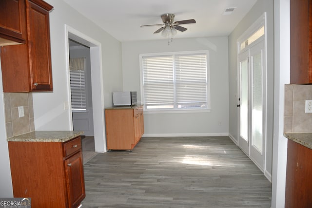 kitchen featuring dark hardwood / wood-style floors, ceiling fan, light stone countertops, and decorative backsplash