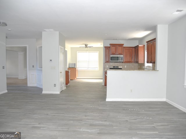 kitchen featuring kitchen peninsula, light stone counters, light hardwood / wood-style flooring, and ceiling fan