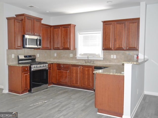 kitchen with light stone countertops, light wood-type flooring, backsplash, stainless steel appliances, and sink