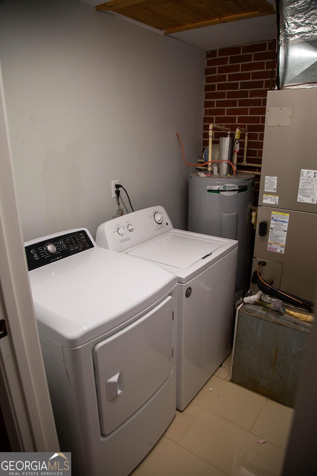 clothes washing area featuring washing machine and clothes dryer, brick wall, and water heater