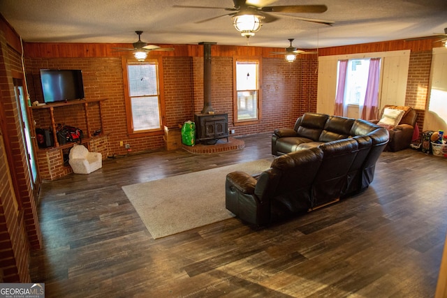 living room featuring a textured ceiling, dark hardwood / wood-style floors, brick wall, and a wood stove