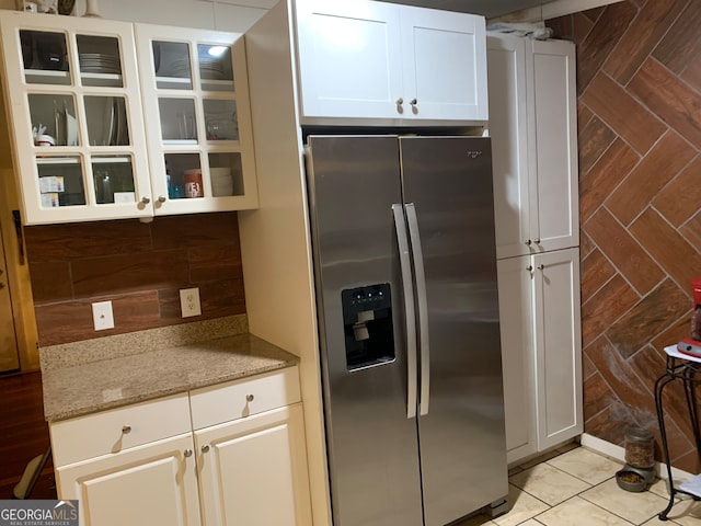 kitchen with light stone countertops, stainless steel refrigerator with ice dispenser, white cabinetry, and light tile patterned flooring