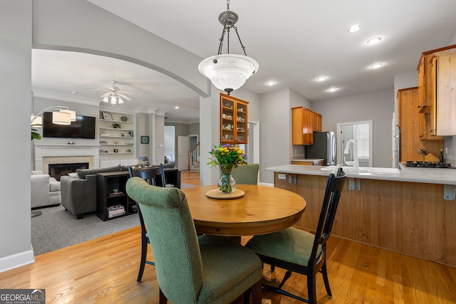 dining space featuring ornamental molding, built in shelves, ceiling fan, sink, and light hardwood / wood-style flooring