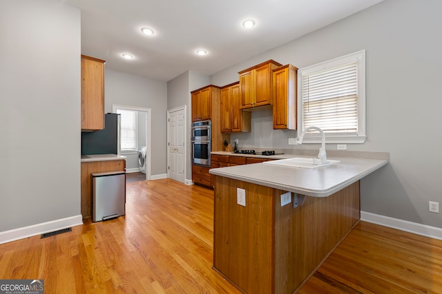 kitchen featuring kitchen peninsula, double oven, washer / dryer, light hardwood / wood-style floors, and black stovetop