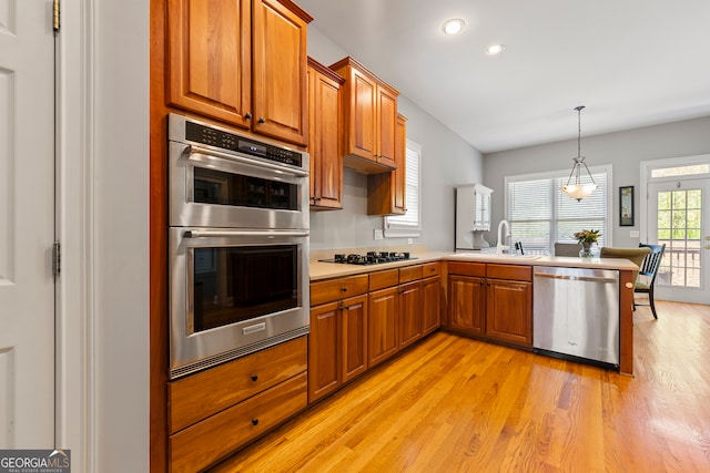 kitchen featuring kitchen peninsula, appliances with stainless steel finishes, light wood-type flooring, sink, and hanging light fixtures