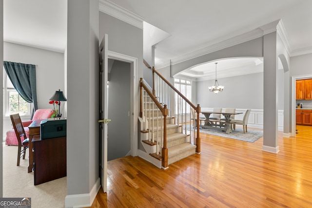 stairway featuring hardwood / wood-style floors, crown molding, and an inviting chandelier