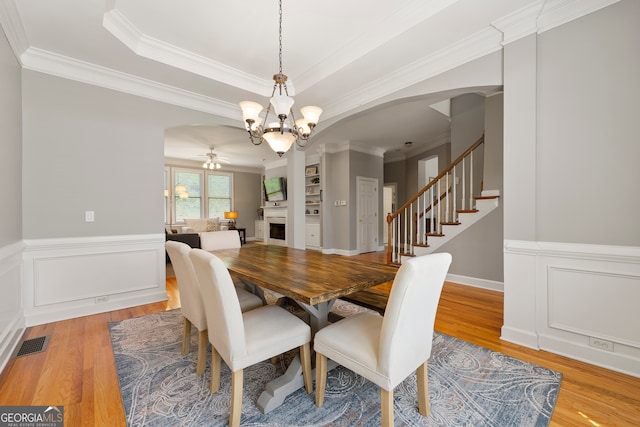 dining space featuring wood-type flooring, ceiling fan with notable chandelier, and ornamental molding