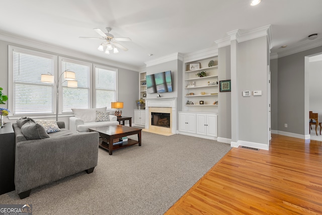 living room with built in shelves, hardwood / wood-style flooring, ceiling fan, and crown molding