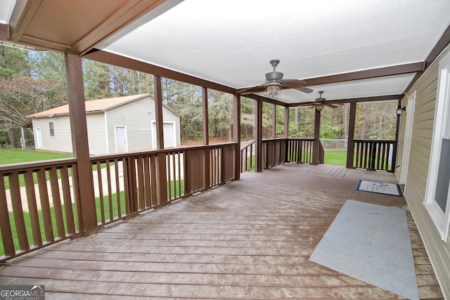 wooden deck featuring ceiling fan, a garage, and an outbuilding