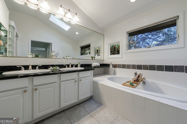 bathroom with tiled bath, vaulted ceiling with skylight, vanity, and tile patterned flooring