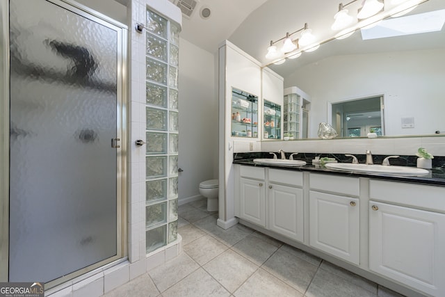 bathroom with tile patterned floors, toilet, vaulted ceiling with skylight, vanity, and a shower with shower door