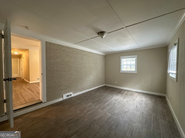 empty room featuring crown molding, dark wood-type flooring, and brick wall