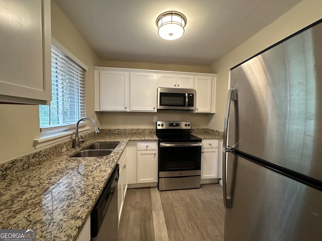 kitchen featuring light stone countertops, white cabinetry, sink, light hardwood / wood-style flooring, and appliances with stainless steel finishes