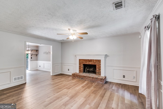 unfurnished living room featuring ornamental molding, a textured ceiling, ceiling fan, light hardwood / wood-style flooring, and a fireplace