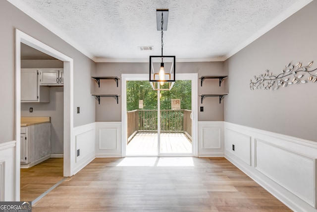 unfurnished dining area with ornamental molding, a textured ceiling, and light wood-type flooring