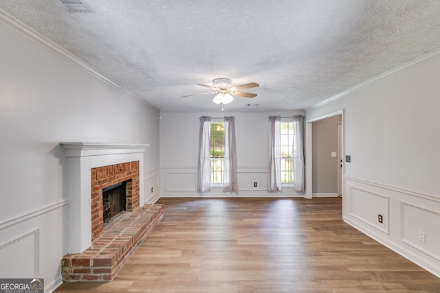 unfurnished living room with light wood-type flooring, a brick fireplace, a textured ceiling, ceiling fan, and crown molding