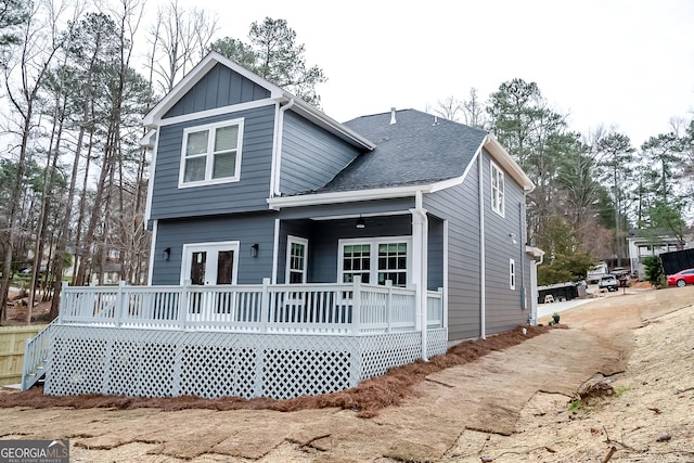 rear view of property with a deck, board and batten siding, and roof with shingles