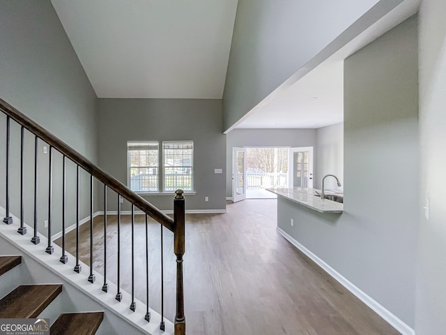 stairway with high vaulted ceiling, wood finished floors, and baseboards