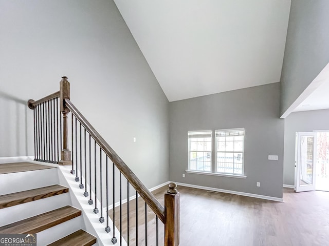 staircase featuring baseboards, high vaulted ceiling, a wealth of natural light, and wood finished floors