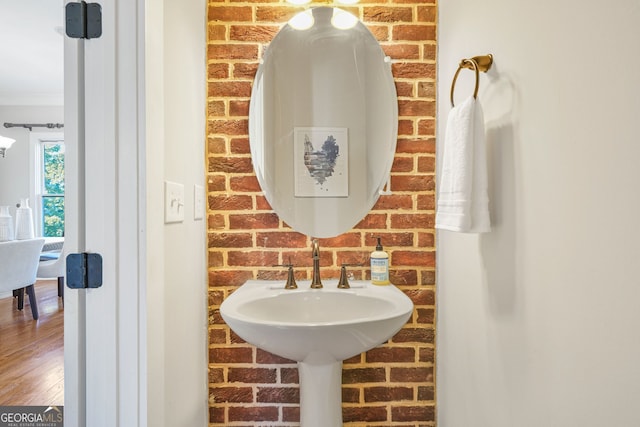 bathroom with hardwood / wood-style floors, crown molding, and brick wall