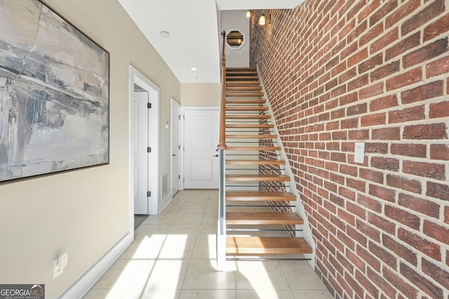 stairs with tile patterned floors and brick wall