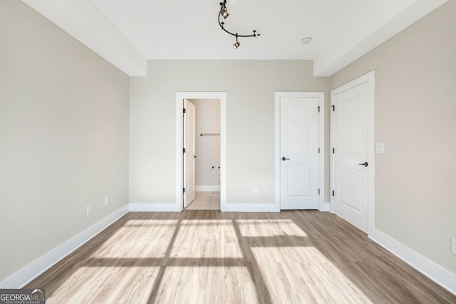 unfurnished bedroom with a spacious closet, a closet, light wood-type flooring, and ensuite bath