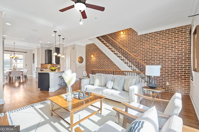 living room featuring ceiling fan with notable chandelier, light wood-type flooring, ornamental molding, and brick wall