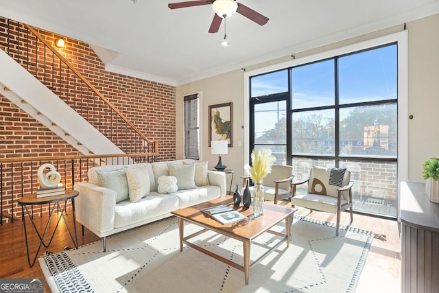 living room featuring ceiling fan, crown molding, wood-type flooring, and brick wall