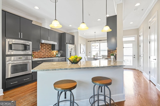 kitchen with hanging light fixtures, kitchen peninsula, a breakfast bar, appliances with stainless steel finishes, and light wood-type flooring