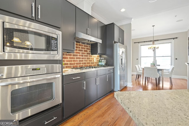 kitchen with hanging light fixtures, light hardwood / wood-style flooring, backsplash, appliances with stainless steel finishes, and ornamental molding