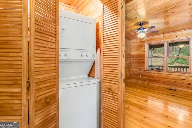 clothes washing area with wood ceiling, ceiling fan, stacked washing maching and dryer, and wooden walls