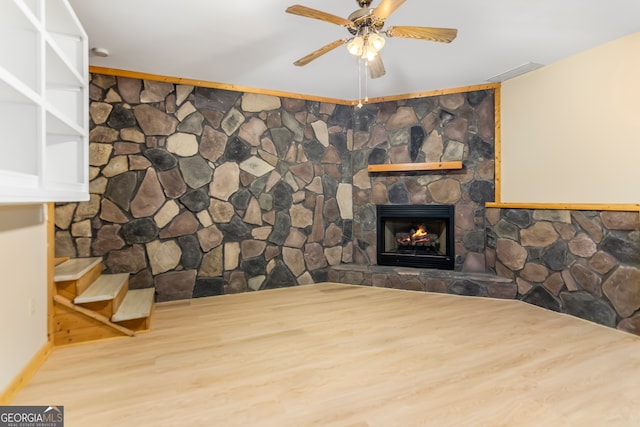 interior space featuring hardwood / wood-style floors, ceiling fan, and a stone fireplace