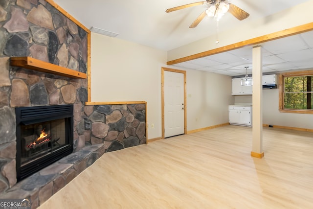 basement featuring a stone fireplace, ceiling fan, and light wood-type flooring