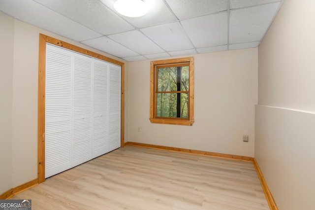 unfurnished bedroom with a drop ceiling, light wood-type flooring, and a closet