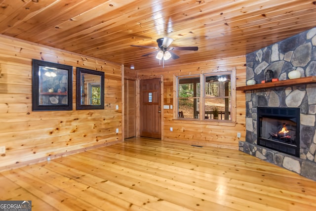 unfurnished living room with hardwood / wood-style flooring, ceiling fan, a stone fireplace, and wooden walls