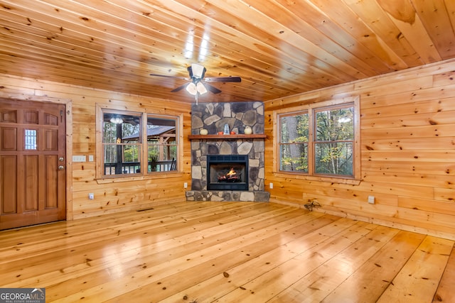 unfurnished living room with a fireplace, light wood-type flooring, wooden walls, and wood ceiling