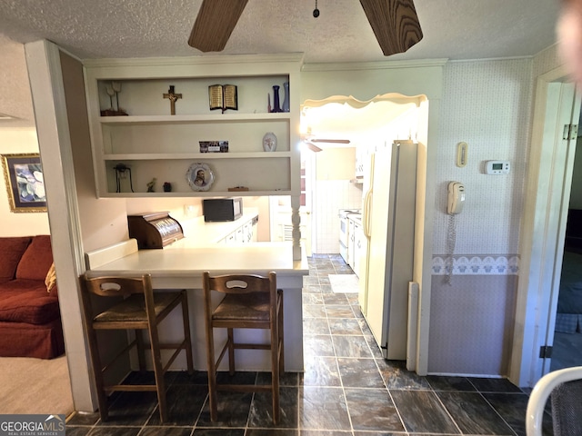 interior space featuring a breakfast bar, ceiling fan, white appliances, and a textured ceiling