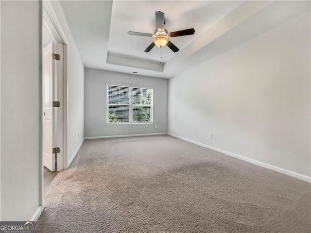 empty room with ceiling fan, light colored carpet, and a tray ceiling