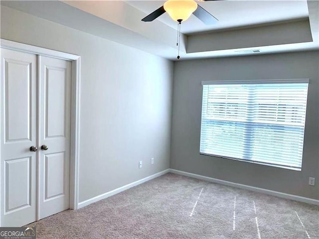 spare room with light carpet, a tray ceiling, and ceiling fan